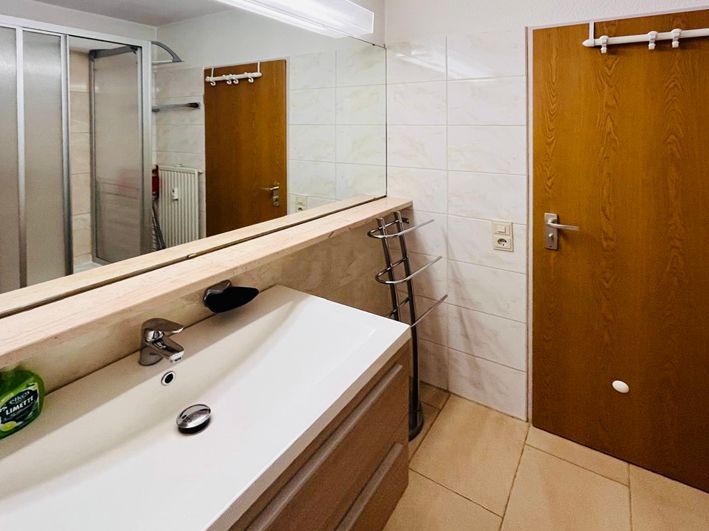 Bathroom with vanity, mirror, shower, and closed wooden door; beige tile.