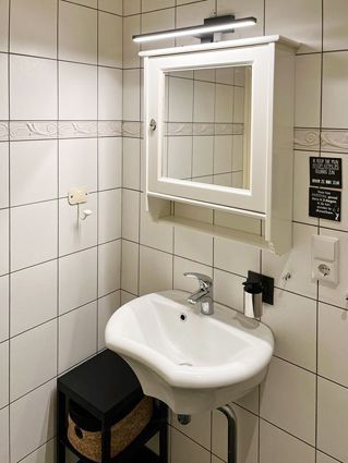 Small white bathroom with sink, mirror cabinet, and black stool.