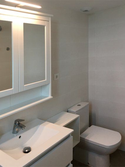 White bathroom with a sink, toilet, and mirror cabinet.