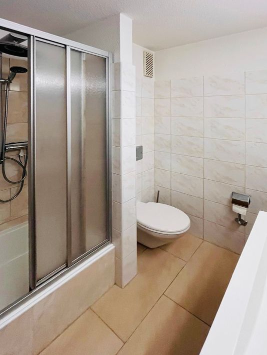 Bathroom with shower, toilet, and light-colored tiles.
