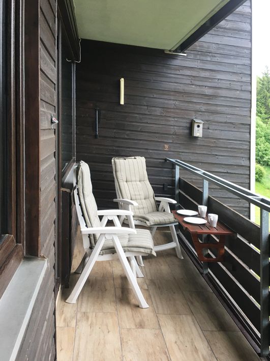 Balcony with two chairs and small table; dark wood siding.