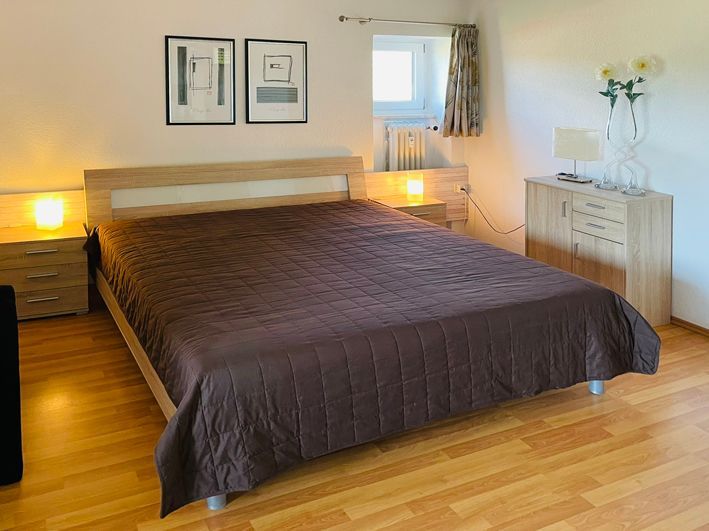 Bedroom with a brown bedspread, nightstands, dresser, artwork, and window with curtains.