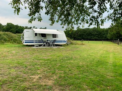 Caravan parked on grassy field, table and chairs set up. Trees in the background, overcast sky.