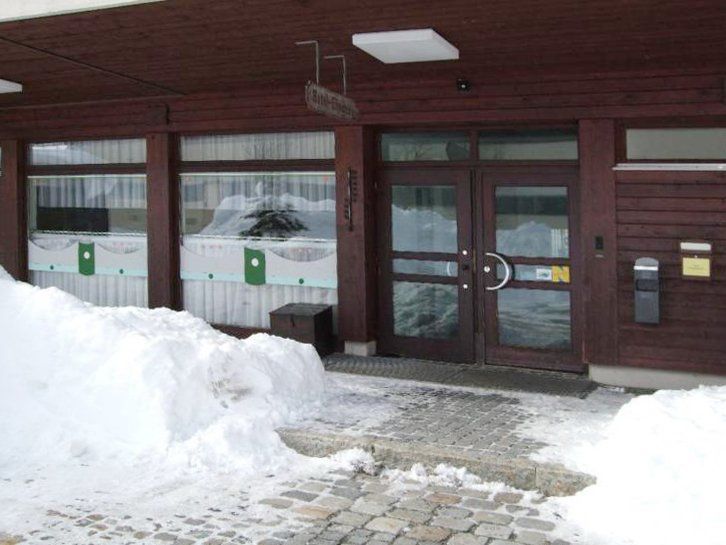 Snowy entrance to a building with wooden siding and a sign above the door.