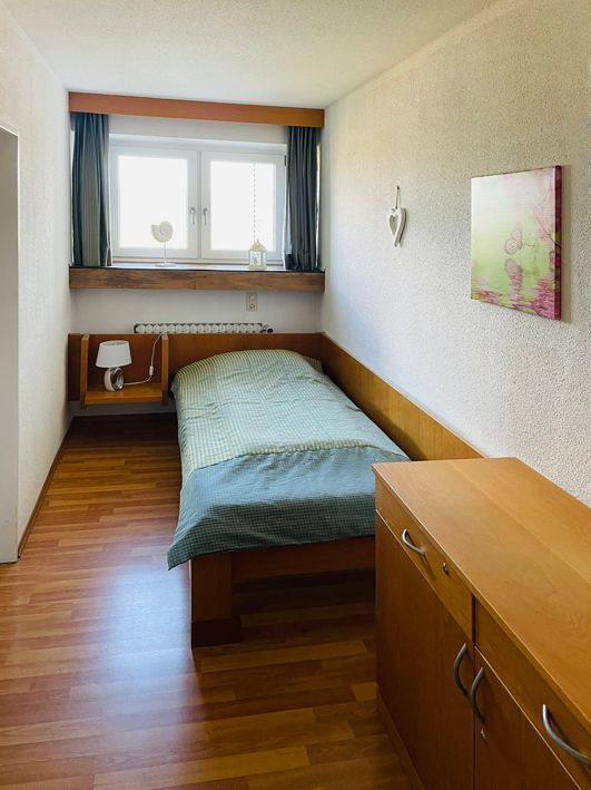 Small bedroom with a single bed, nightstand, dresser, and window with curtains.