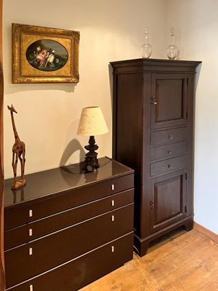 A room corner with dark furniture: a dresser, cabinet, and art on the wall with a lamp and giraffe statue.
