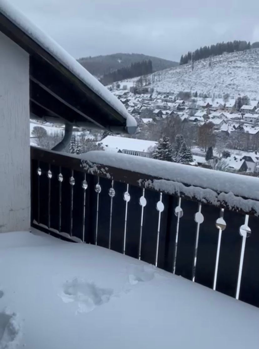 Snow-covered balcony overlooking a village nestled in a snowy valley with a mountain backdrop.