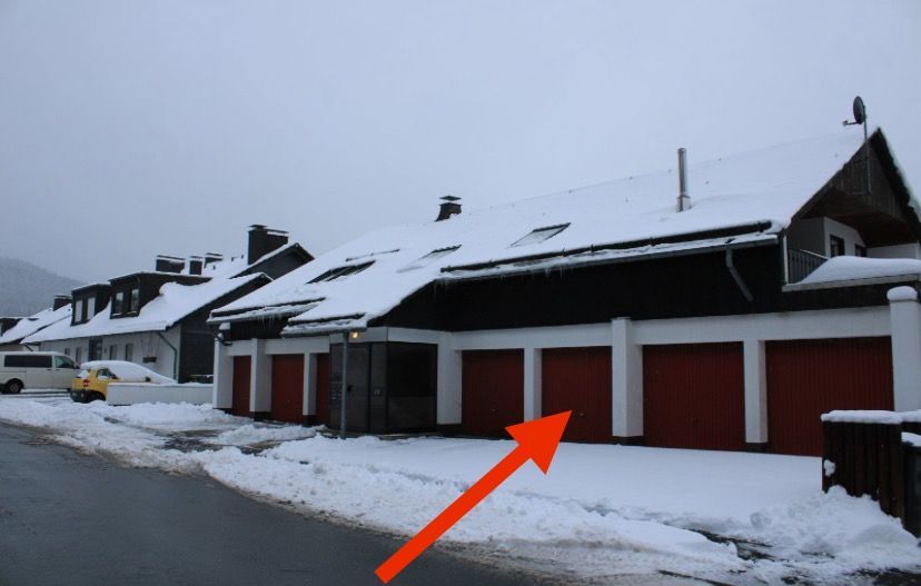 Building with red garage doors, snow-covered roof and ground, set in winter.