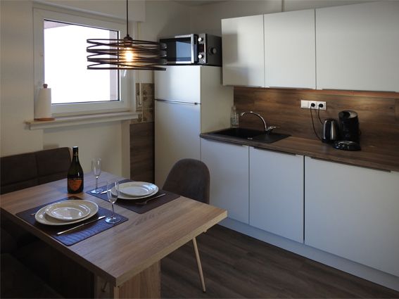 Small modern kitchen with white cabinets, wood accents, and a dining table.