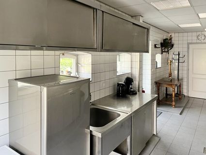 Stainless steel commercial kitchen with sink, counters, and cabinets. White tiled walls, door, and table.