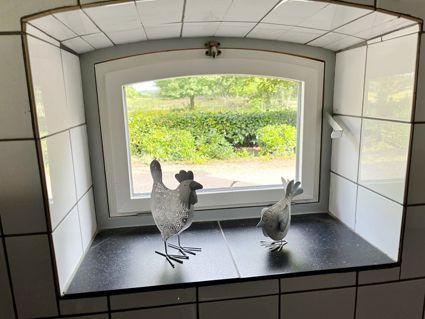 Two metal bird figurines sit in a tiled window. Outside, greenery is visible.