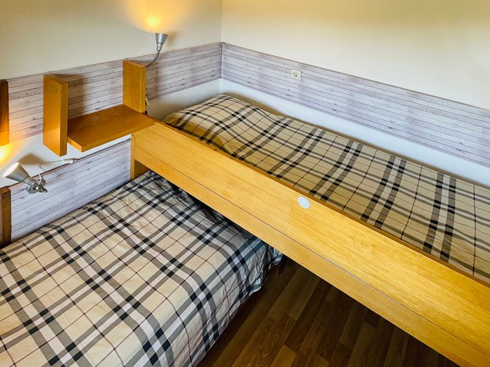 Two beds with plaid bedding in a corner room. Wooden frames, light wood tones.