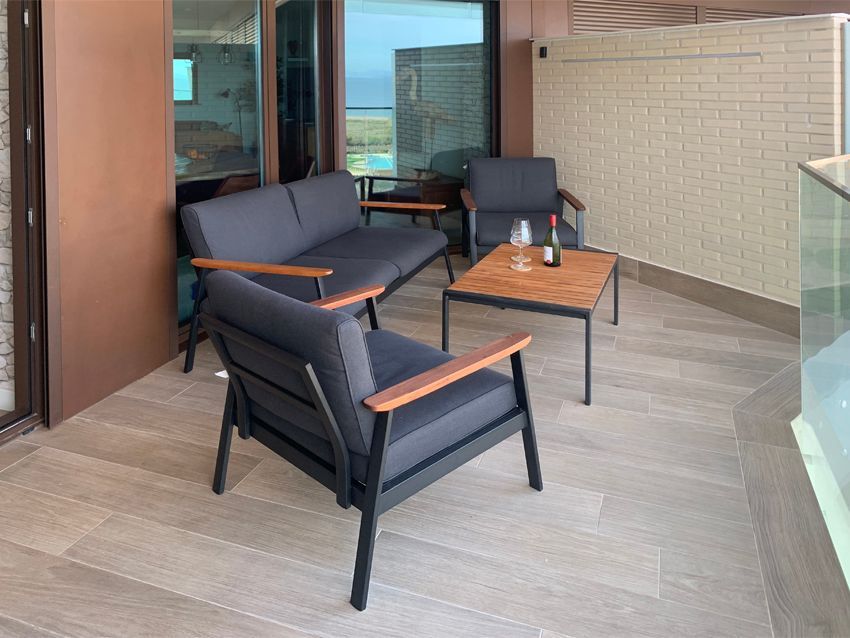 Outdoor seating area: gray cushioned furniture, wooden accents, small table, wine, and view.