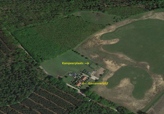 Aerial view of a campsite and building complex next to a swamp and forest.