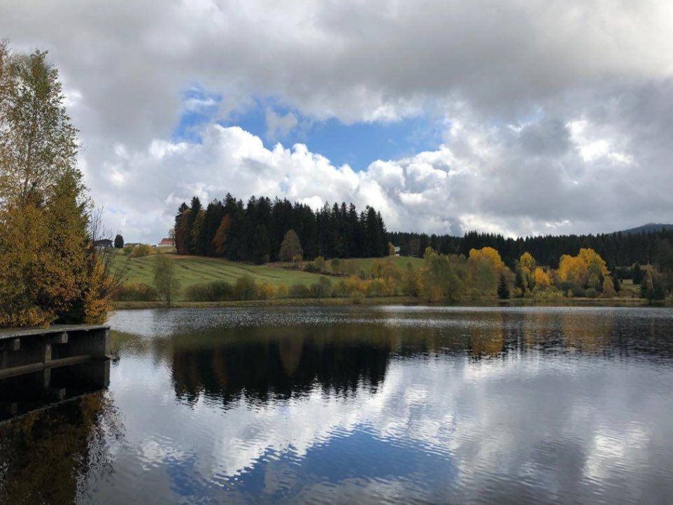Lake with reflections of cloudy sky and fall foliage.