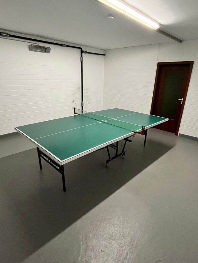 Green ping pong table in a room with a gray floor, white walls, and a brown door.