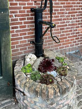 Black water pump on a brick planter filled with succulents and rocks against a brick wall.