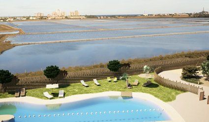 Pool overlooking a salt marsh. Lounge chairs on grass. Buildings in the distance.