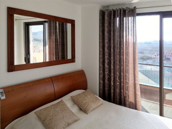 Bedroom with bed, mirror, brown curtains, and a view through a sliding glass door.