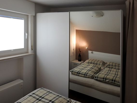Bedroom with a white wardrobe, one side mirrored, reflecting bed and window.
