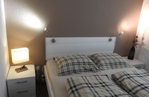 Bedroom with a white headboard, plaid bedding, two nightstands, and wall lamps.