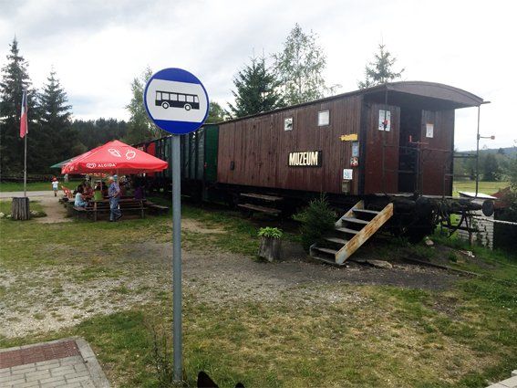 A repurposed train car, used as a building, sits near a bus stop sign and outdoor seating area.