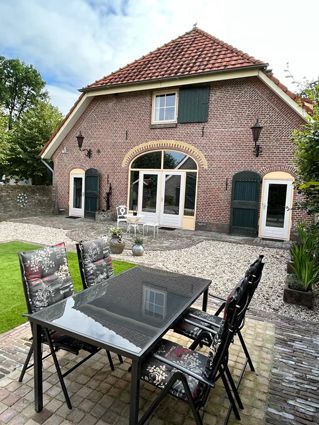 Back patio with table and chairs in front of a brick building with white doors, green shutters, and a red tile roof.