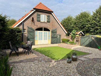 Brick barn with open green shutters and door, small lawn, table, and gravel patio.