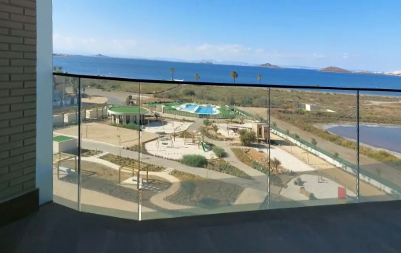 View from a glass balcony overlooking a playground, park, and water against a blue sky.
