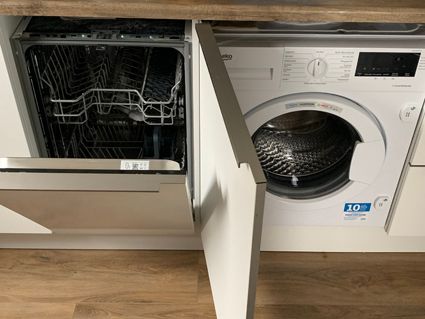 Open dishwasher and washing machine side-by-side in a kitchen cabinet.