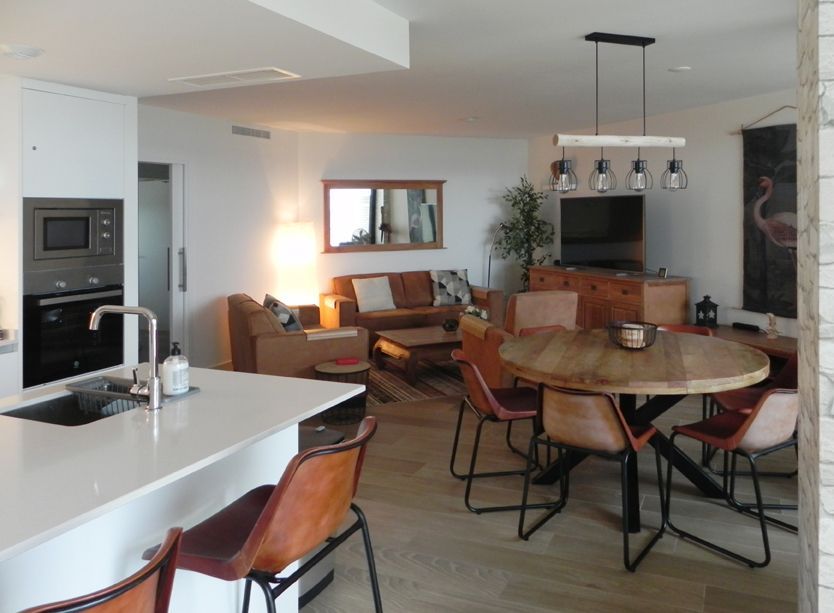 Open-concept living space with kitchen island, dining table, and living room furniture; earth-tone color scheme.