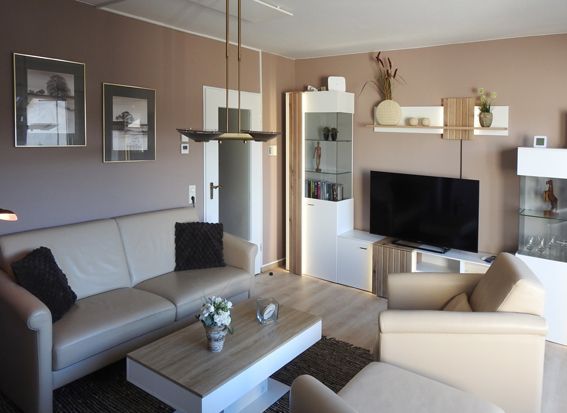 Living room with beige sofa, white furniture, brown walls, and a television.