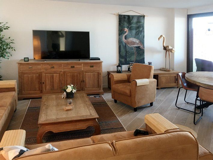 Living room with wooden furniture: TV, sideboard, coffee table, sofa, armchair, and flamingo décor.