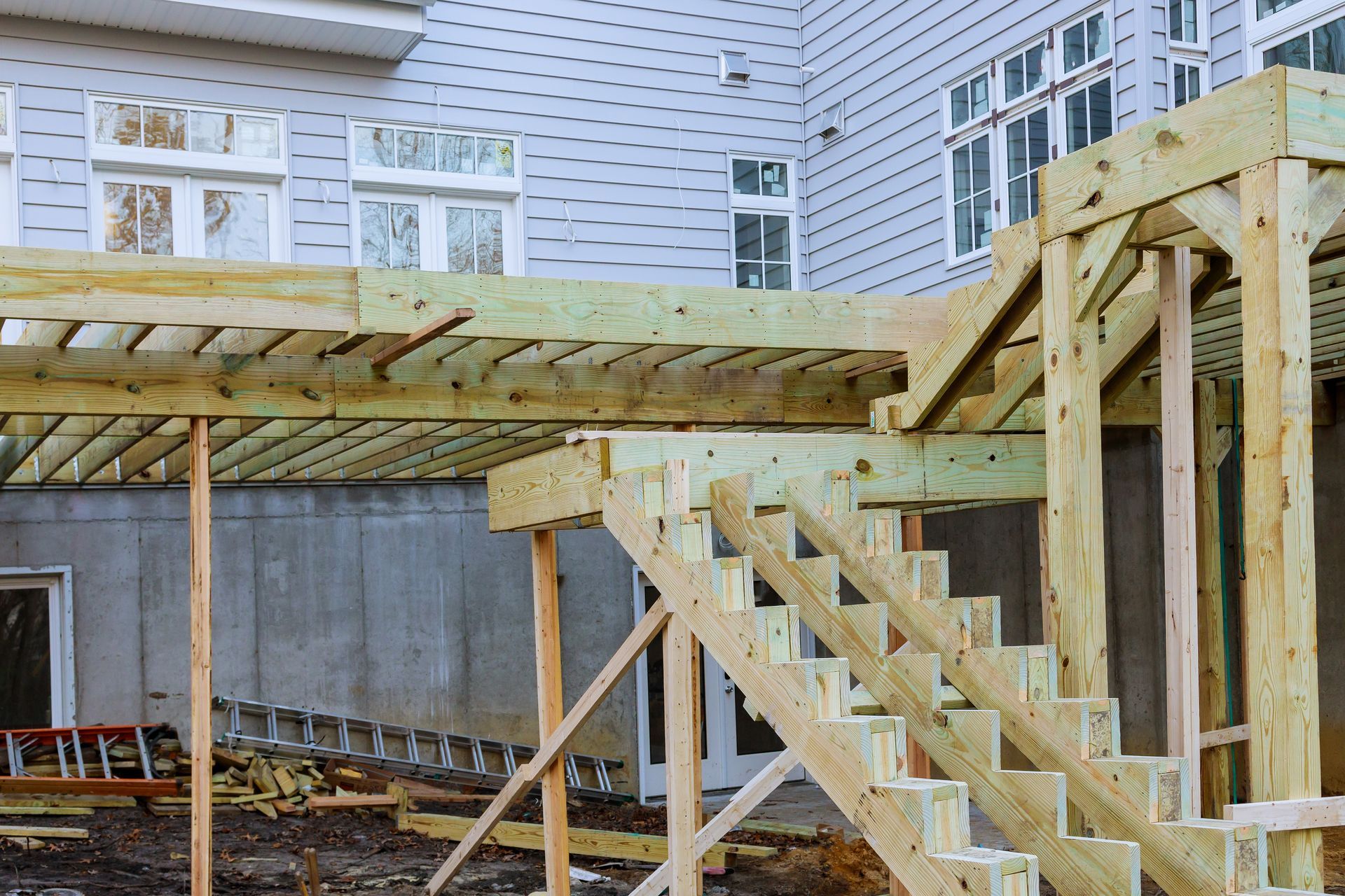 Unfinished wooden deck with stairs being built adjacent to a gray house.