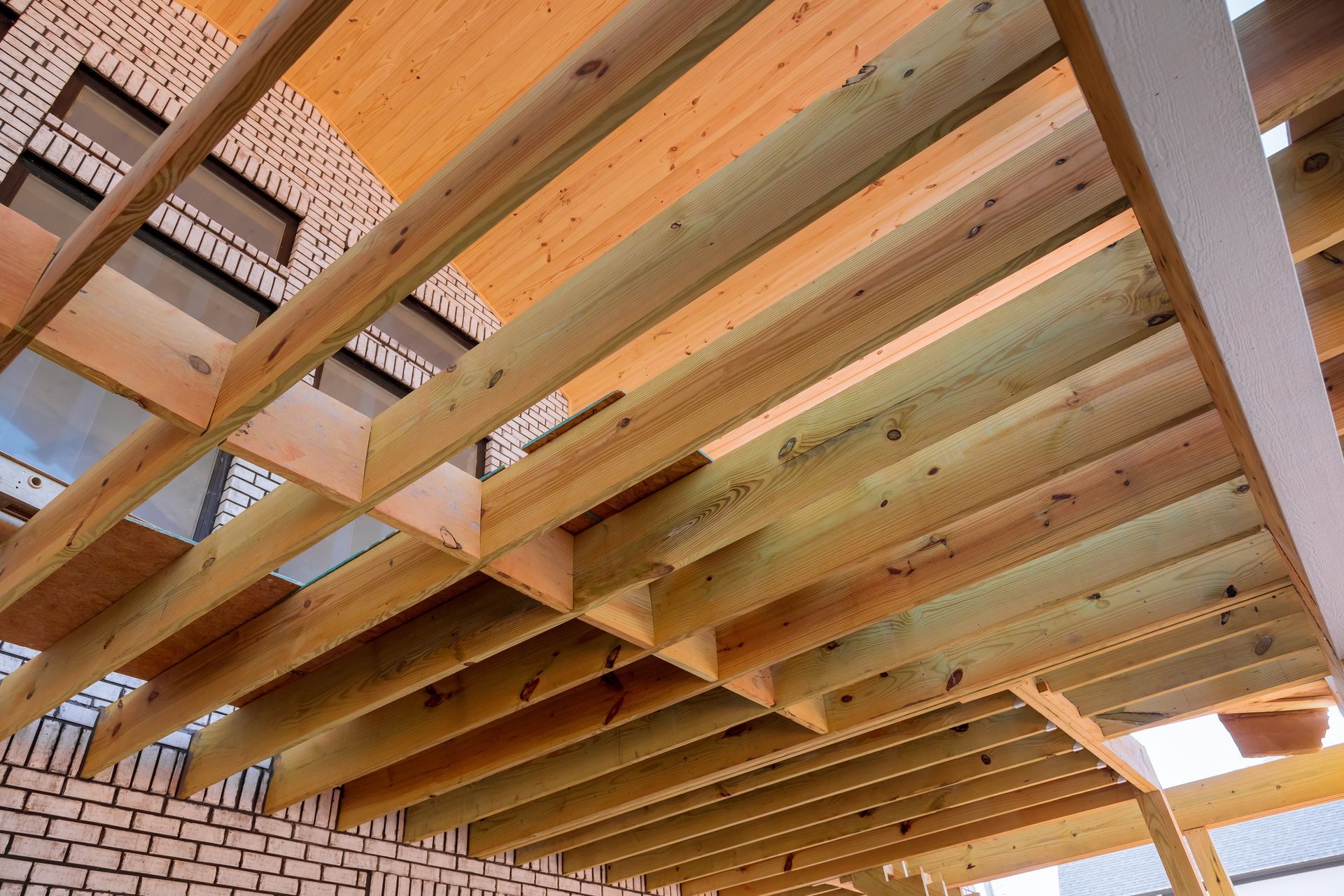 Wooden deck structure, viewed from below, against a brick building; natural wood tones.