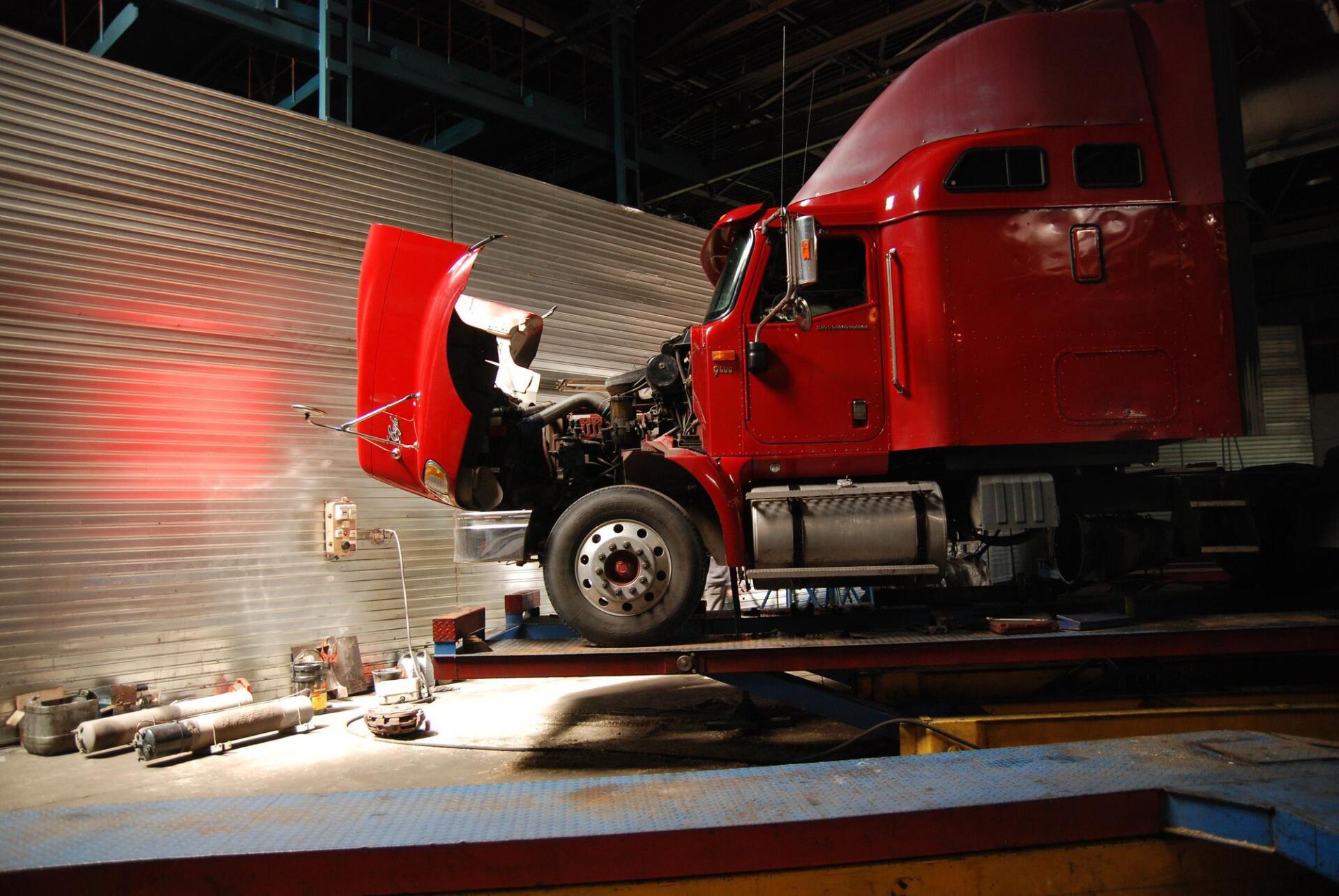 A red semi truck is sitting on a lift with its hood open