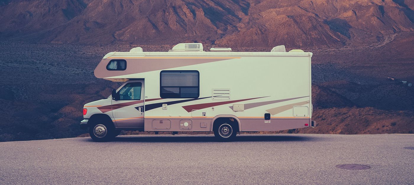 A rv is parked on the side of the road in front of a mountain.