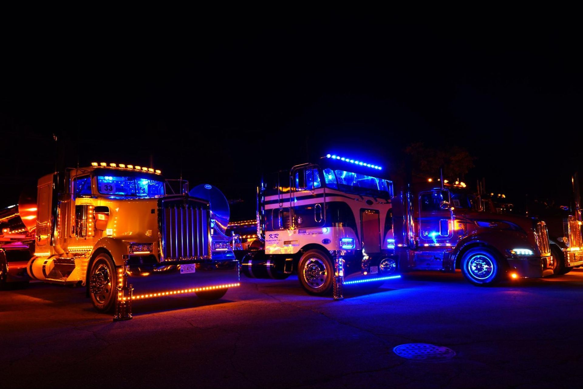 Three semi trucks are parked next to each other in a parking lot at night.