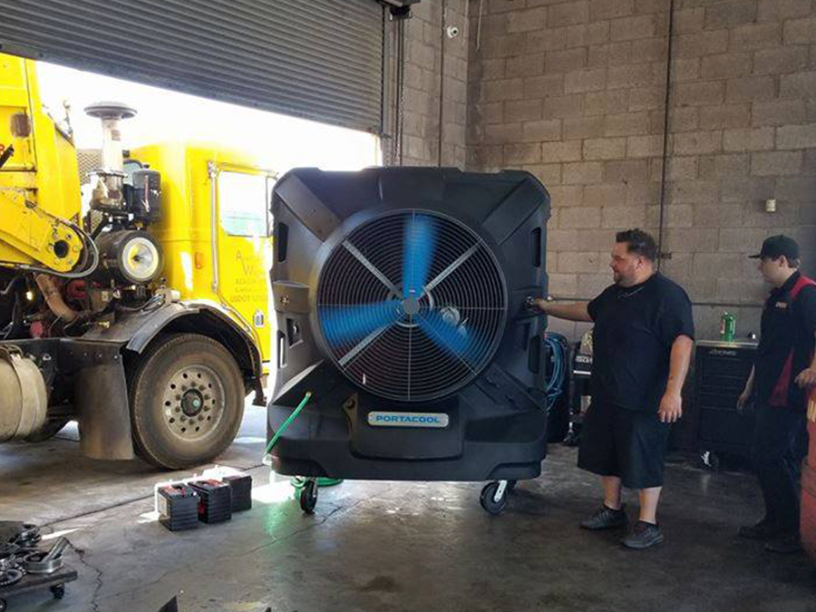 Two men are carrying a large fan in front of a truck.