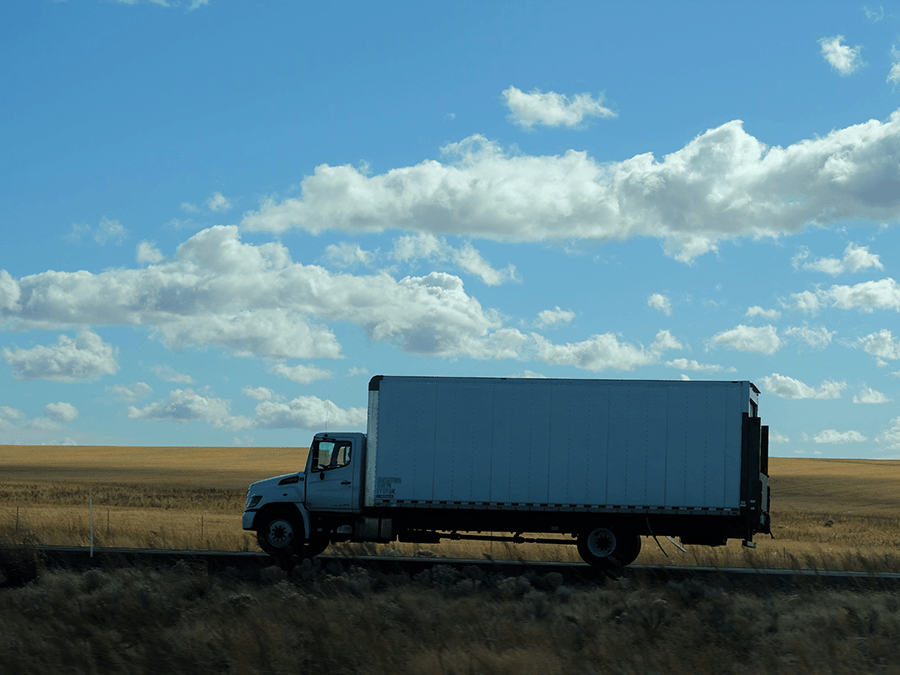 A white truck is driving down a road in the middle of a field