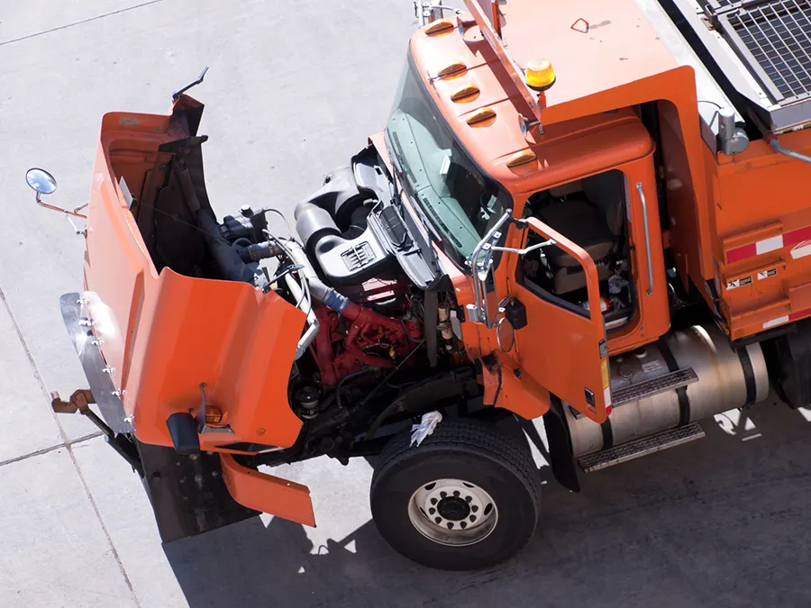 An orange truck with its hood open is parked on the side of the road