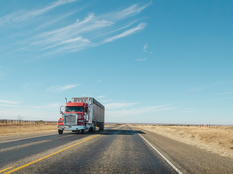 A red semi truck is driving down a highway.