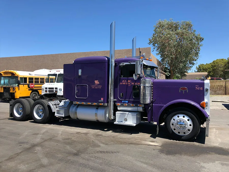 Purple semi truck parked in a lot, side view with chrome exhaust stacks and sleeper cab