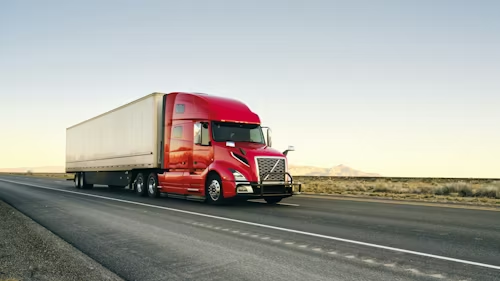 Red semi-truck hauling a white trailer on a пуст desert highway at sunset