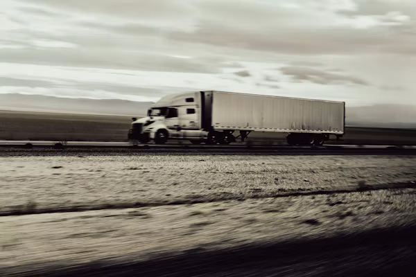 Semi-truck with white trailer driving on a flat, snowy roadside under a cloudy sky