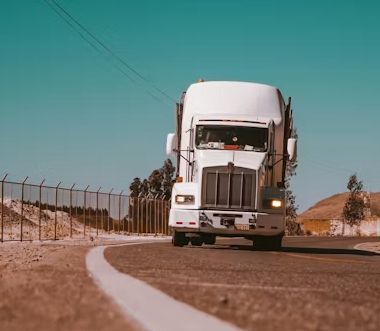 White semi-truck driving on a curving rural road under a clear blue sky