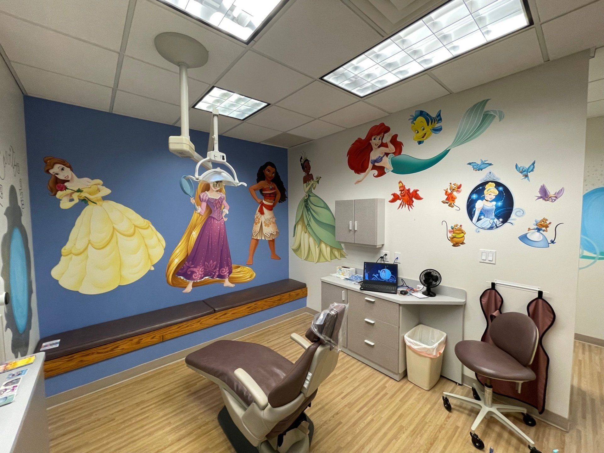 A dental office with a dental chair and a mural of princesses on the wall.