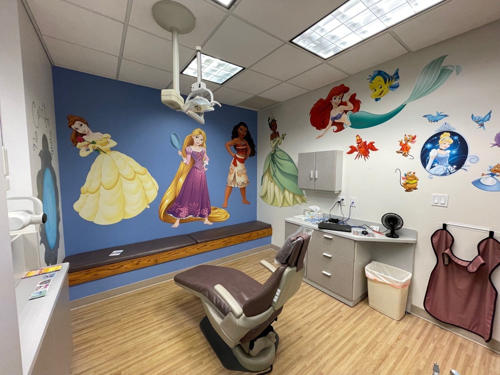 A dental office with a dental chair and a mural of princesses on the wall.