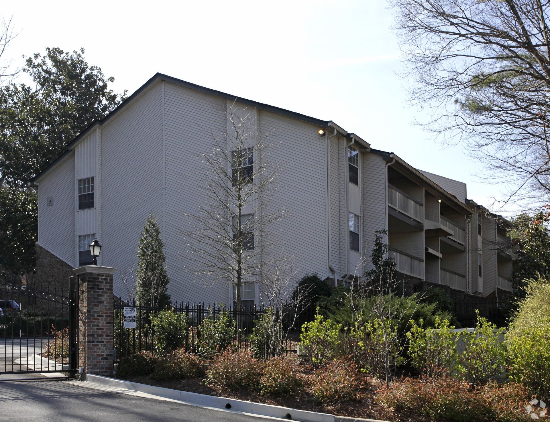 Multi-story tan apartment building with balconies, behind a brick and wrought iron gate.