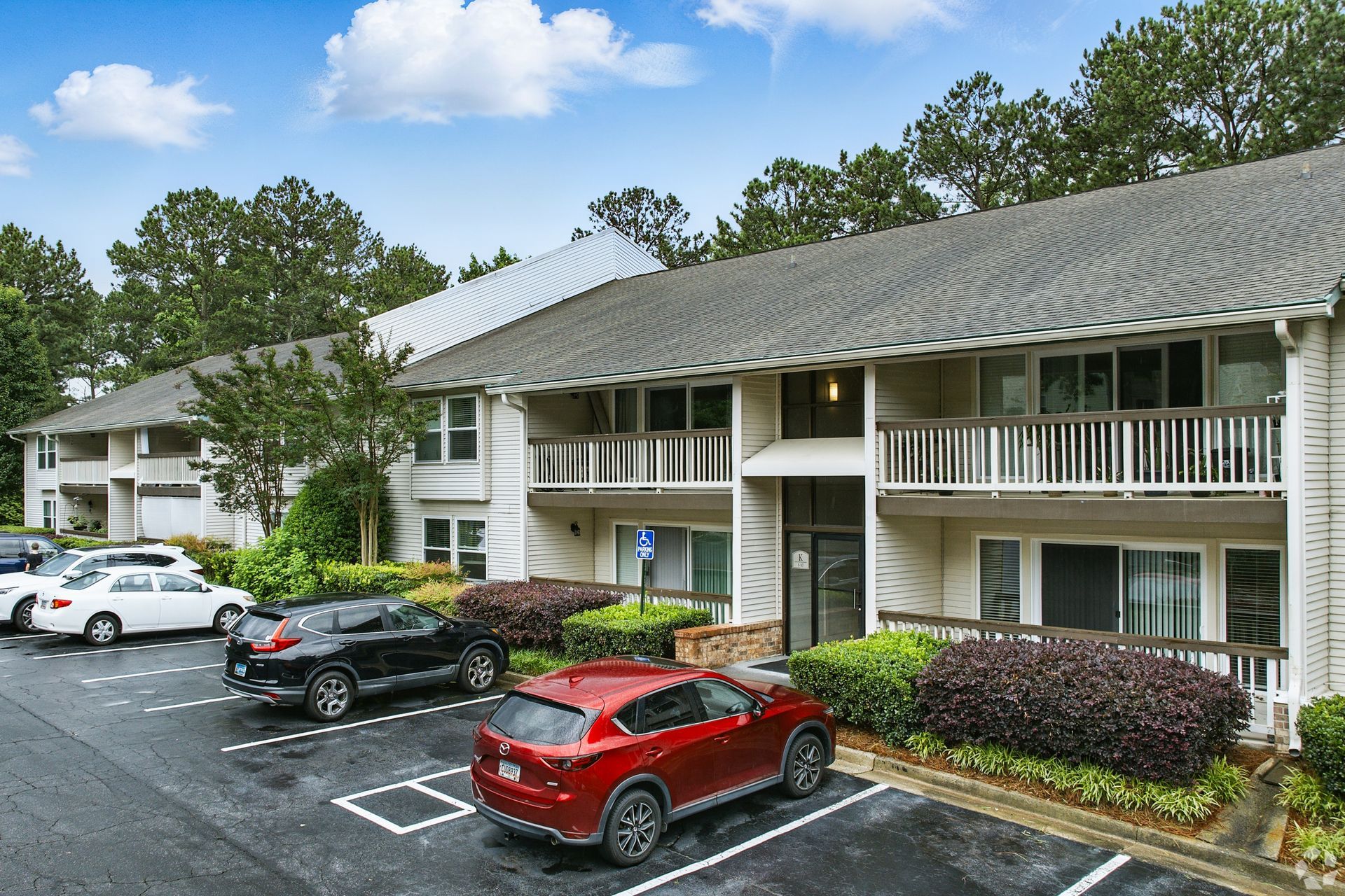 Apartment building with cars parked out front, accessible parking spot, and surrounding greenery.